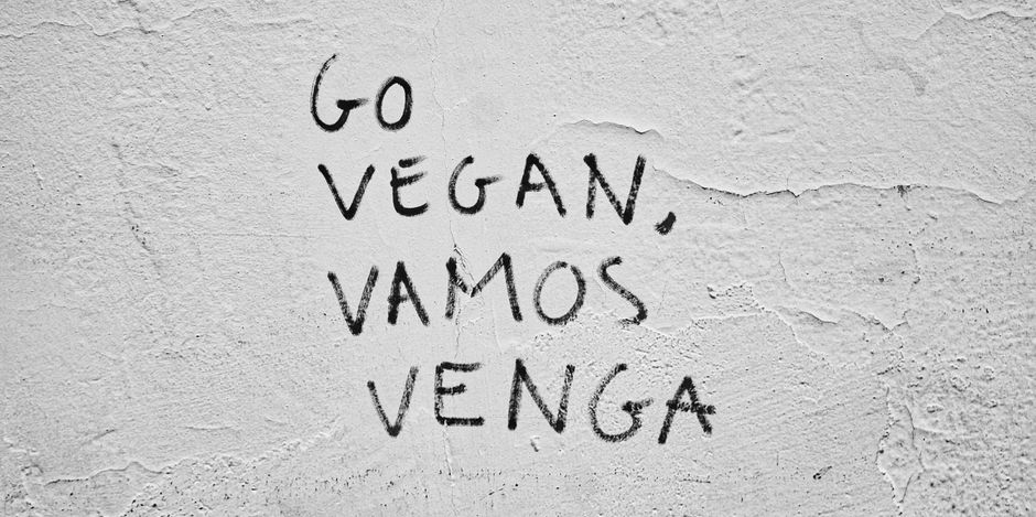 Grafiti negro 'Ve al Vegano, Vamos Venga' en una pared texturizada promueve el veganismo.
