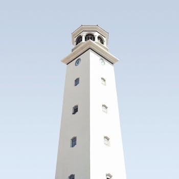 A minimalist white clock tower with geometric details set against a clear blue sky.