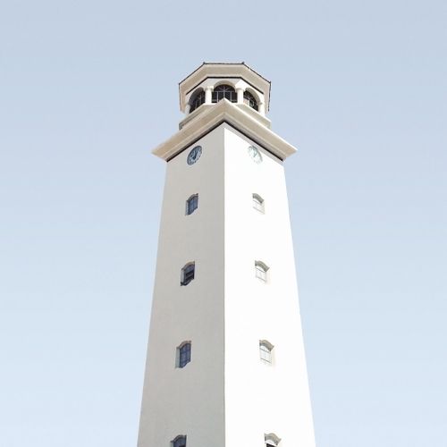Free A minimalist white clock tower with geometric details set against a clear blue sky. Stock Photo