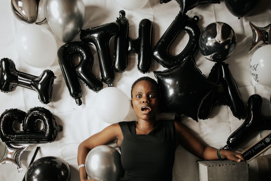A surprised black woman surrounded by black and white balloons during her birthday celebration.