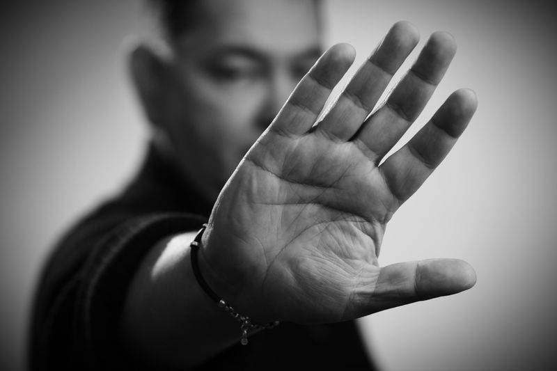 Black and white close-up of a man's hand raised in a stop gesture, focusing on palm details.