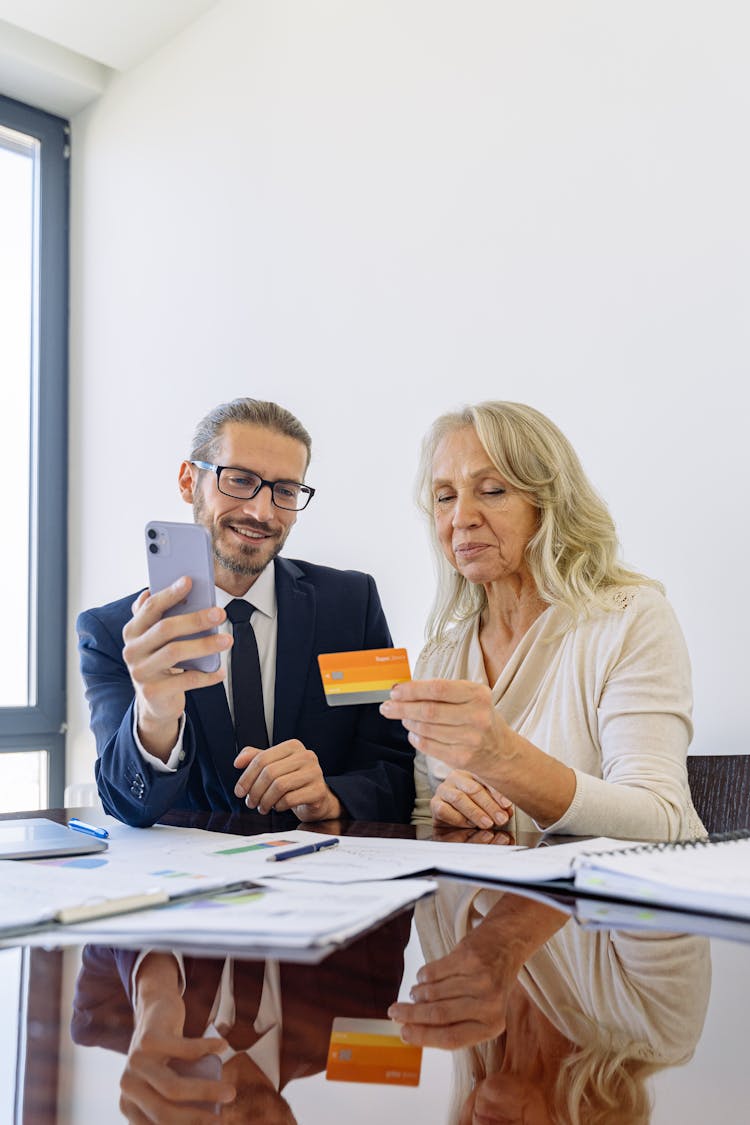 Elderly Woman Holding A Credit Card Beside A Man Holding A Smartphone