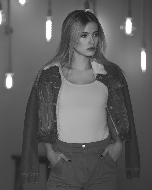 Free Grayscale portrait of a woman in a denim jacket posing indoors with hanging lights. Stock Photo