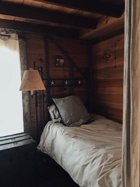 Comfortable single bed with white sheets and cozy pillows in narrow light bedroom in rustic wooden cottage