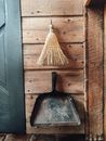 Straw broom and shovel hanging on wooden wall
