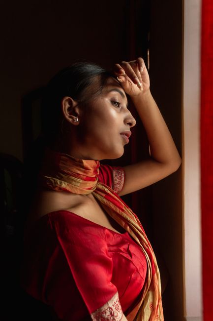 A woman in a traditional saree gazes thoughtfully outside, capturing a moment of introspection.
