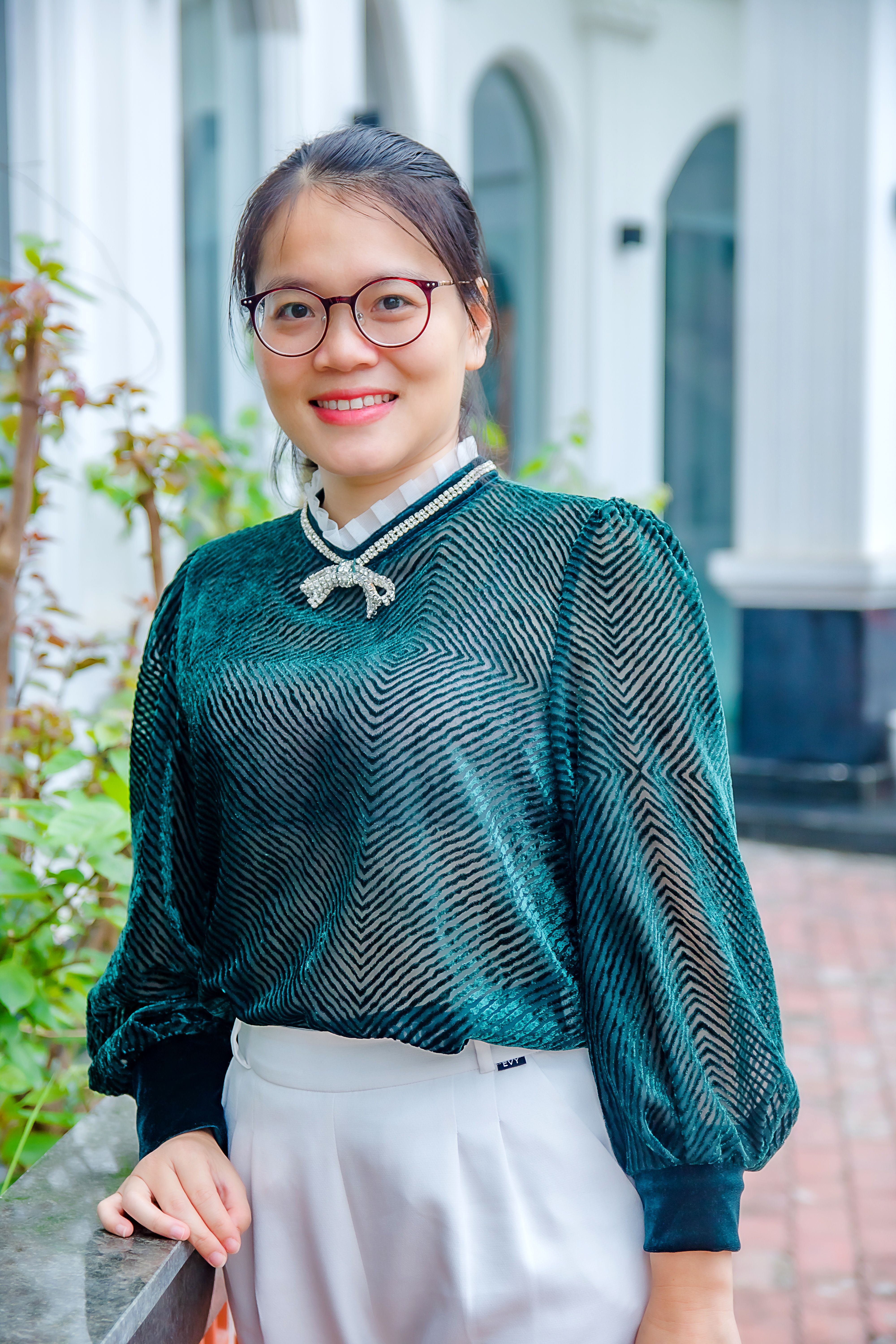 Fashionable Asian woman in eyeglasses and green blouse posing outdoors.
