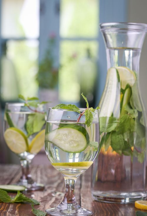 Free Glass of refreshing lemon and cucumber-infused water with mint leaves on a wooden table. Stock Photo