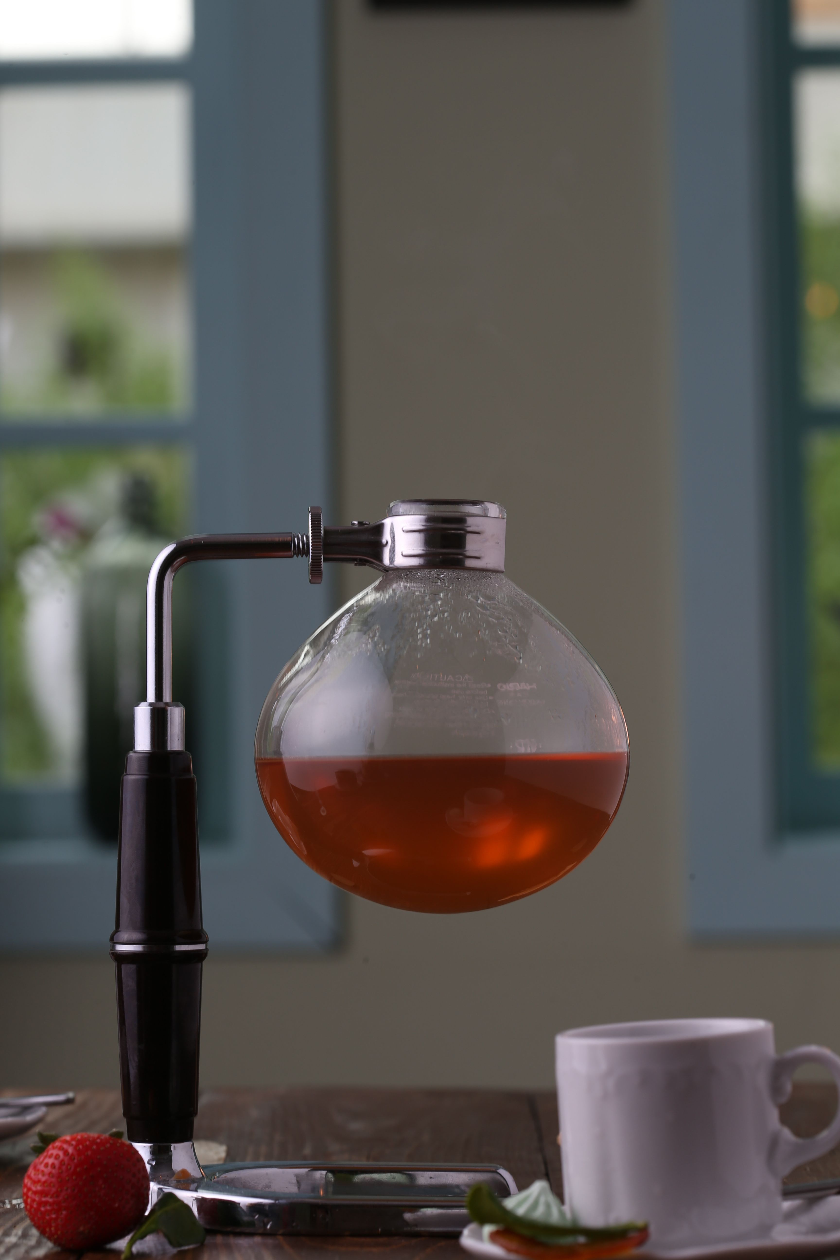 A sophisticated glass siphon coffee maker filled with brewed coffee on a wooden table.