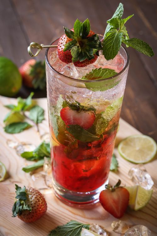 Free Tall glass of strawberry mint mocktail with ice and lime slices on a wooden table. Stock Photo
