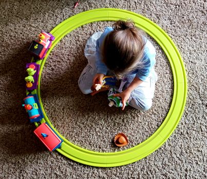 A child playing with colorful toy train and figures on a carpet, viewed from above.