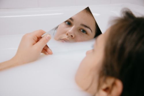 Free A woman lies in a milky bath, holding a mirror reflecting her serene expression. Stock Photo