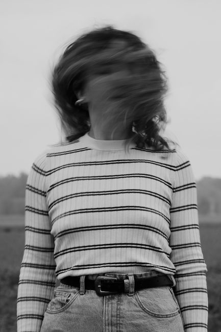 Artistic black and white portrait with motion blurred hair and a striped shirt.