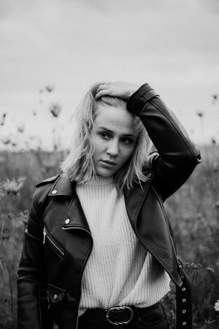 Moody black and white portrait of a woman posing outdoors in a leather jacket.