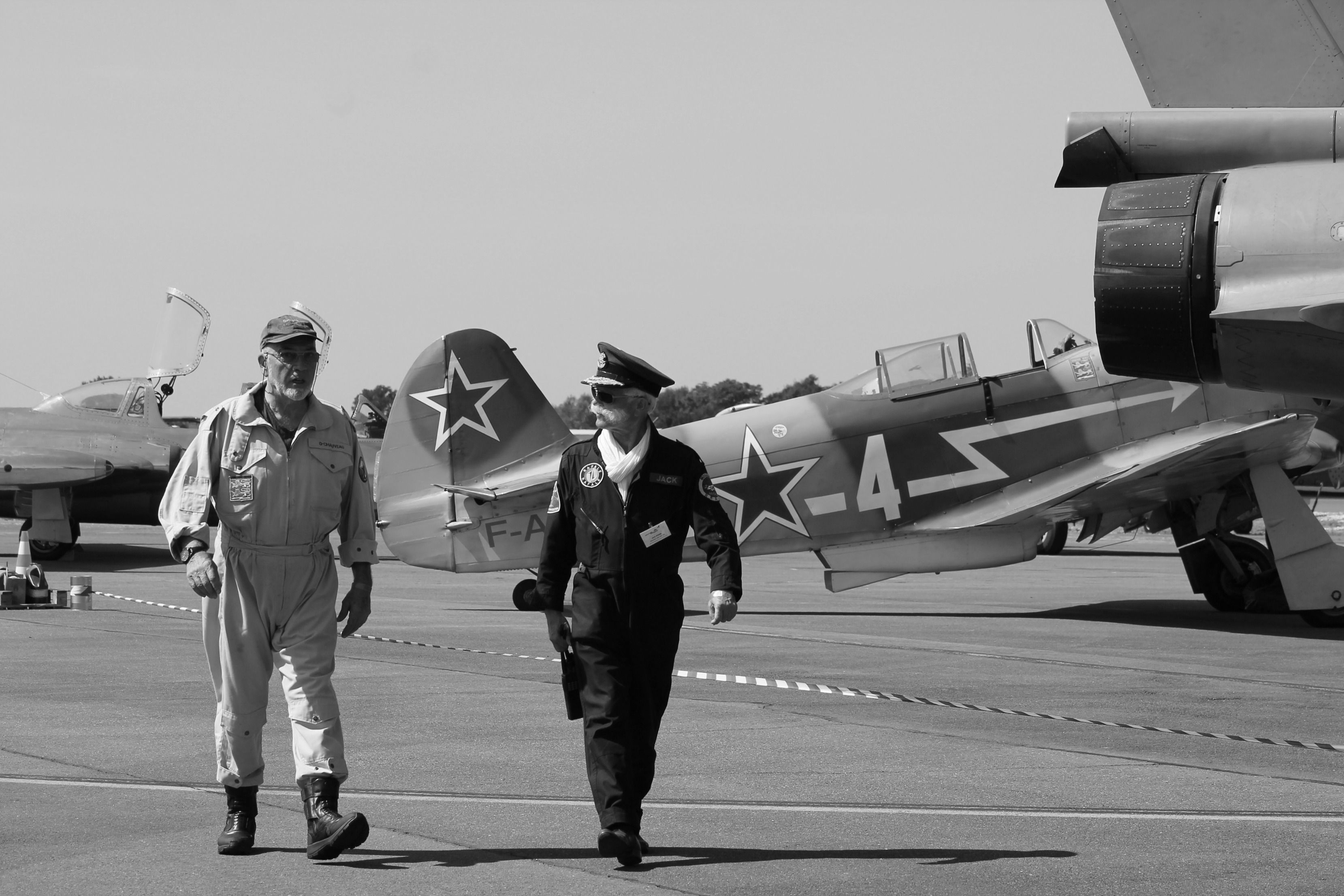 Two men in vintage uniforms walk by Soviet-era fighter jets at an air show.