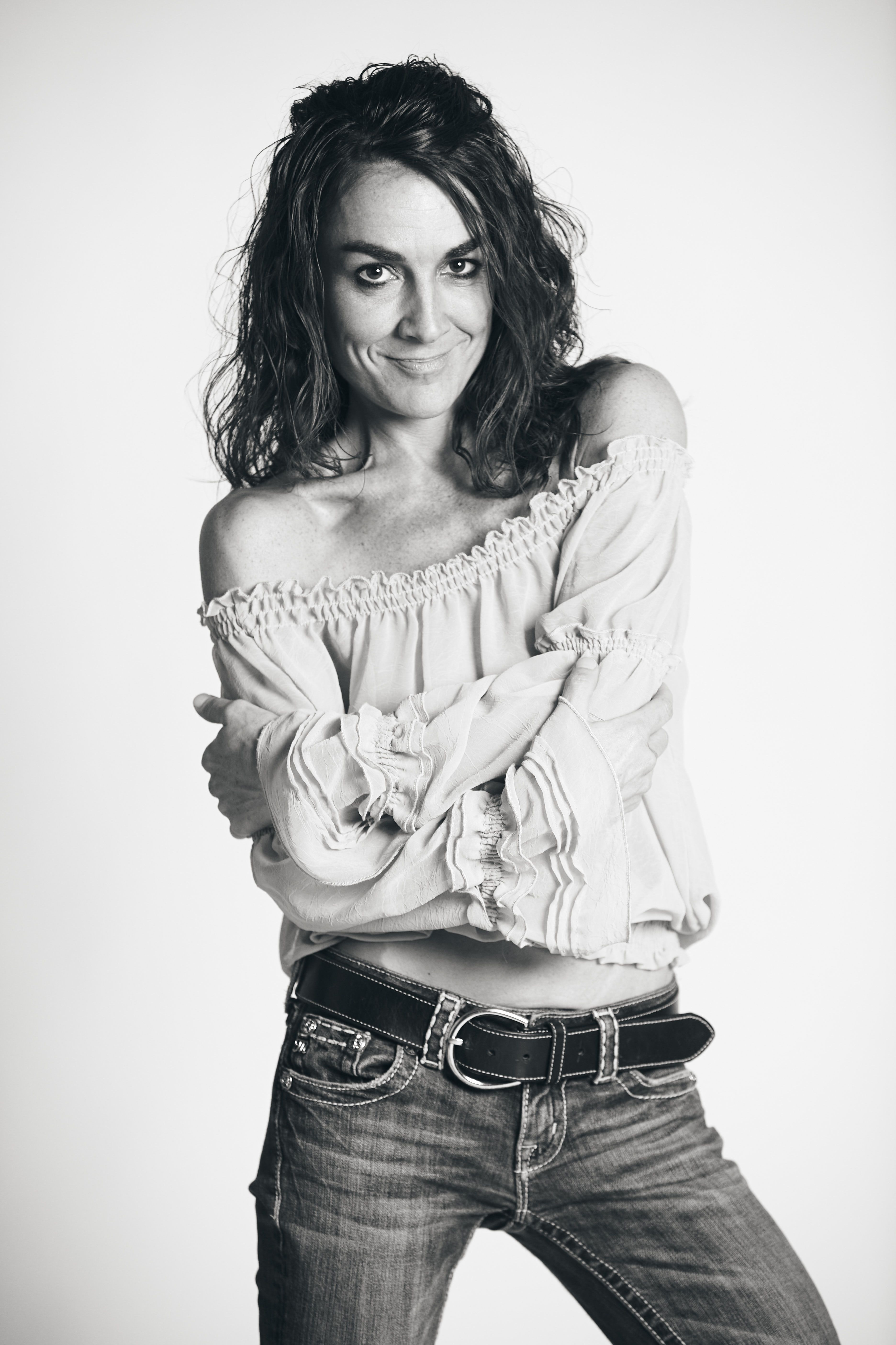Black and white portrait of a smiling woman in casual attire, exuding confidence.