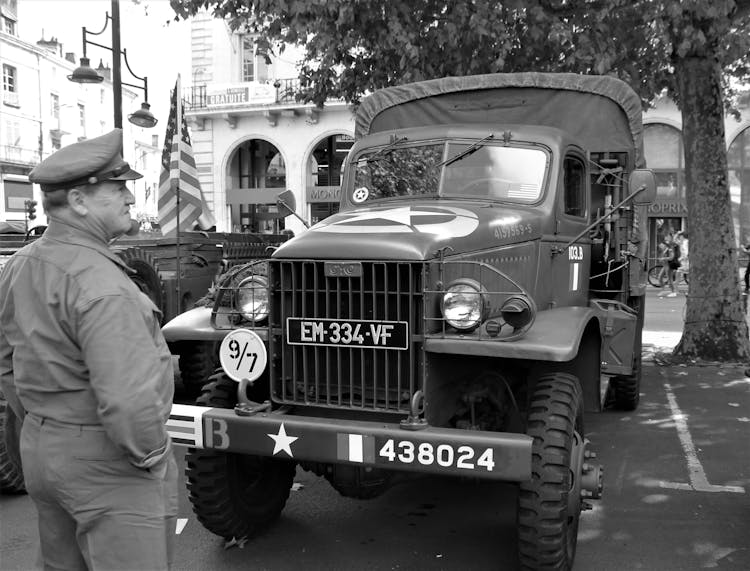 Grayscale Photo Of Man Standing In Front Of A Military Vehicle