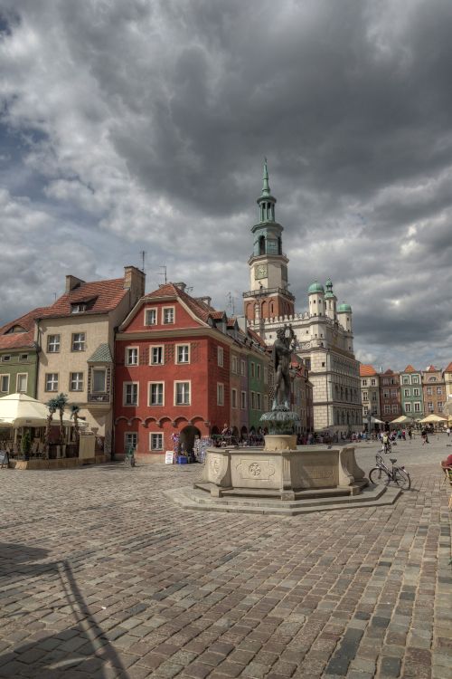 Free Dramatic cloudscape over Poznań's historic market square with colorful buildings and a medieval town hall. Stock Photo