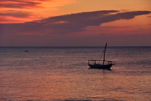 Free A serene seascape at sunset with a silhouetted sailboat on calm waters, evoking tranquility. Stock Photo