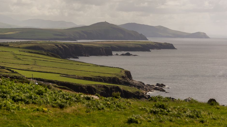 A winding coastal road along the scenic Ring of Kerry in Ireland, with lush green hills and the Atlantic Ocean.