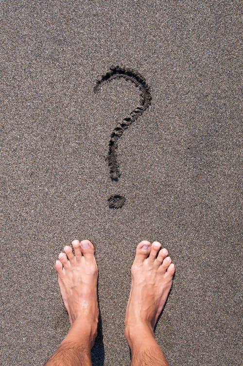 Person Standing on Black Sand Beach in Front of Question Mark