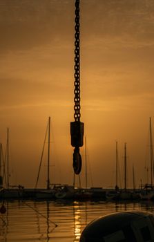 Serene harbor view in Thessaloniki with a chain and yachts silhouetted against a sunset backdrop.