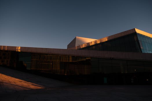 A modern architectural facade at dusk showcasing the Oslo Opera House with elegant glass and stone design.