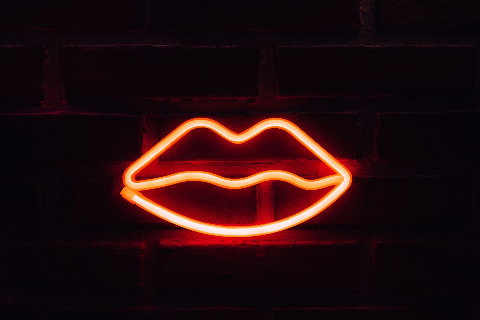 Un neón rojo con forma de labios sobre una pared de ladrillo