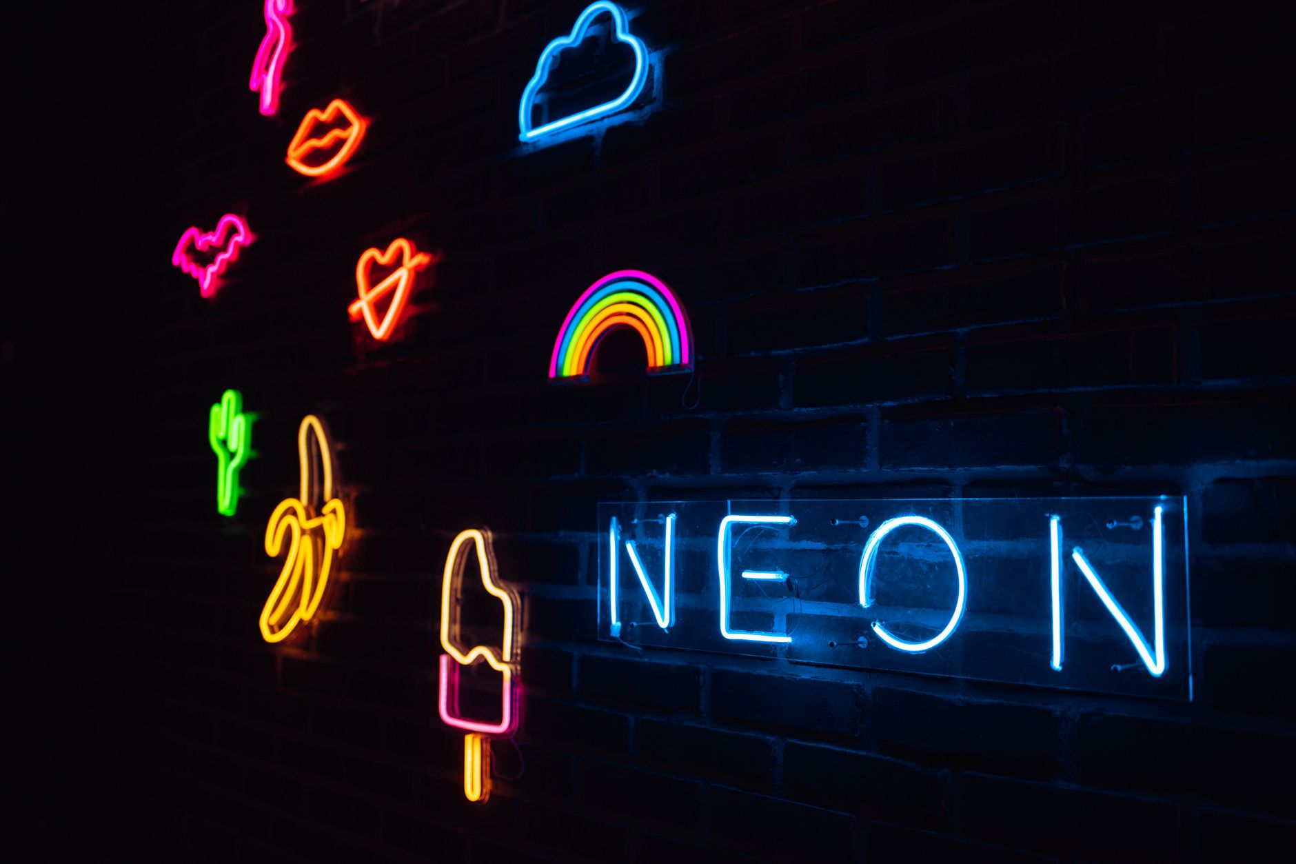 Vibrant neon signs illuminated on a dark brick wall with various shapes and colors.