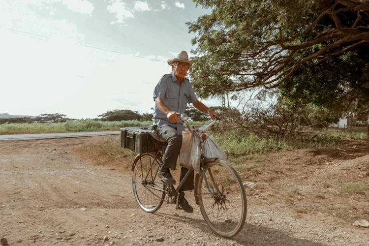 Senior Man Riding Bicycle On Rough Road In Countryside