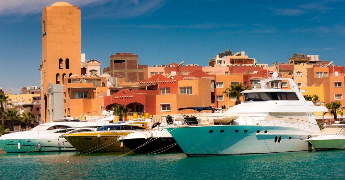 Scenic marina with yachts docked by colorful buildings under blue sky.
