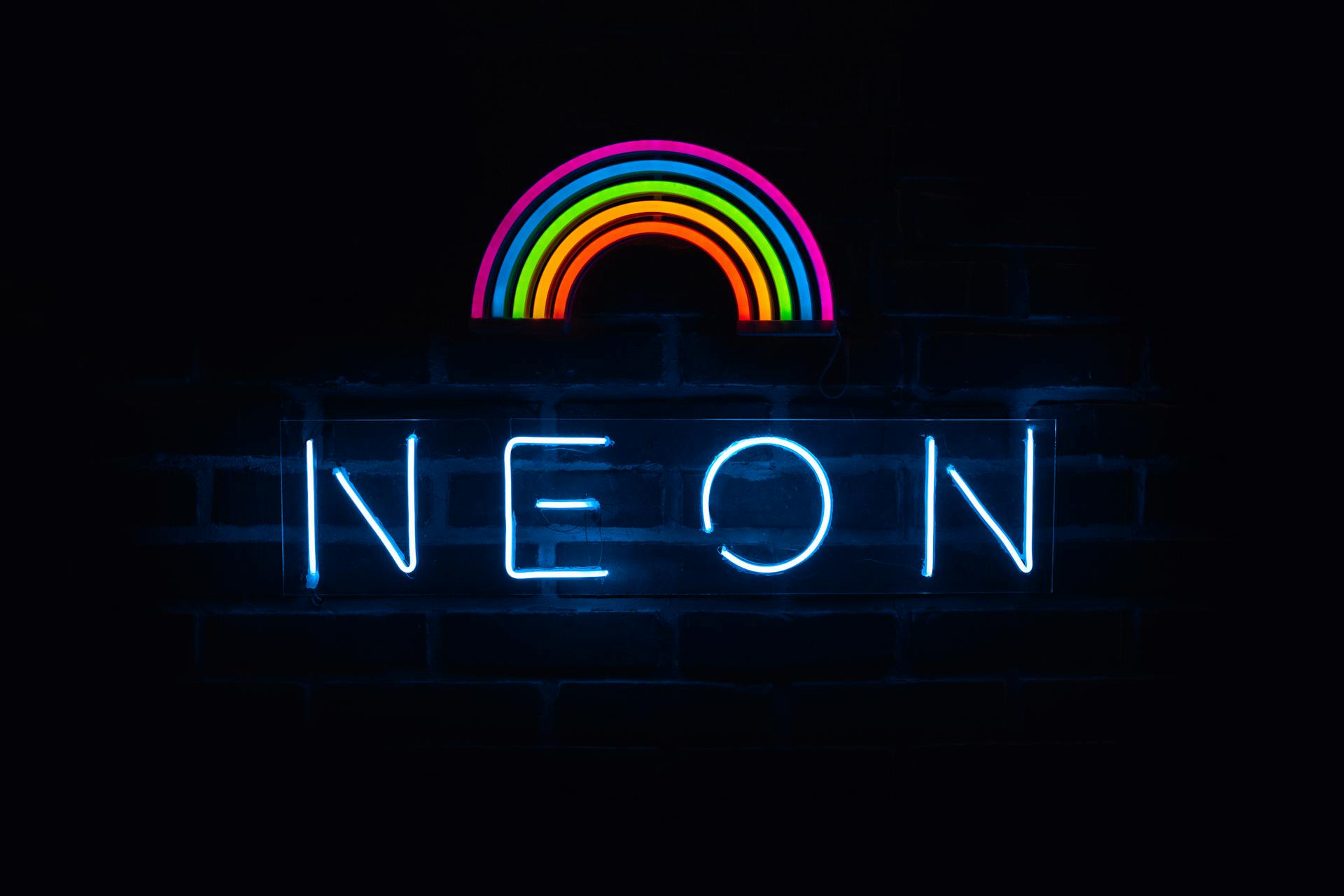Colorful neon rainbow and text sign against a dark backdrop.