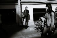 Black and white of passers strolling on paved street near facade of building under sunlight