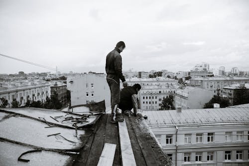 Free Black and white full body of anonymous man changing roof on broken building located in residential area of city Stock Photo