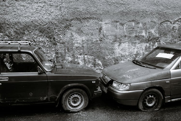 Old Damaged Cars Near Rough Gray Wall