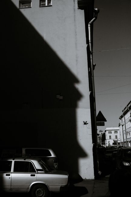 Black and white of aged automobile parked near tall concrete building on street of town