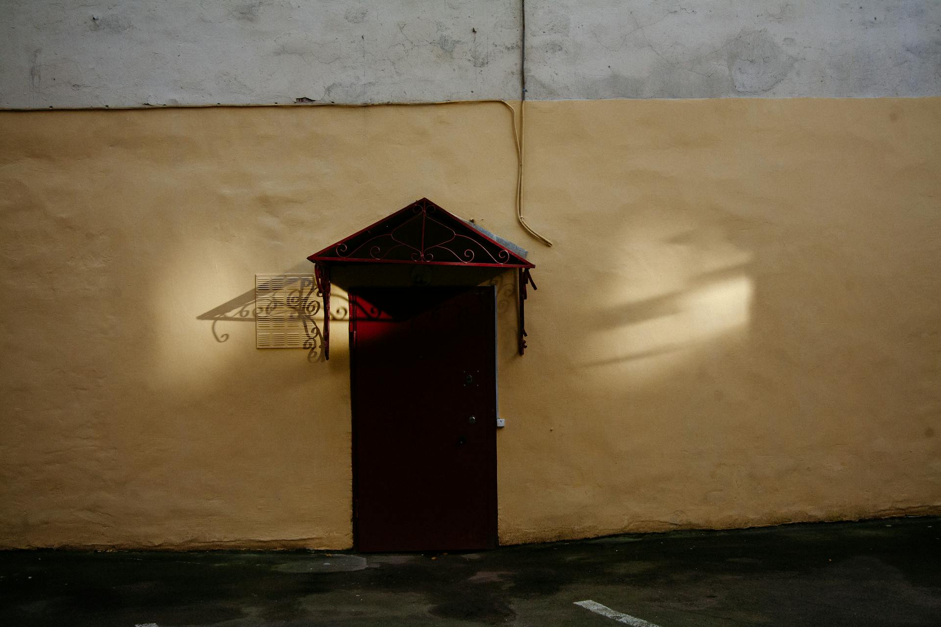 Exterior of aged stone building with electric wires above closed red metal door located on yellow wall on sunny day