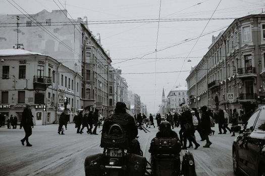 Black and white of people crossing asphalt road while cars and motorcycle with sidecar waiting for permission signal of traffic light in city in daylight