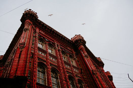 From below of aged masonry lyceum exterior with arched windows and ornamental walls under soaring birds in Istanbul