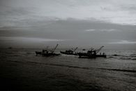Black and white of unrecognizable fishermen on trawling boats with fishing nets on rippled ocean under cloudy sky