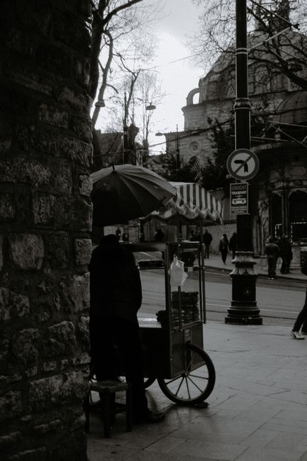 Black and white of anonymous food seller on tiled pavement in city with walking people