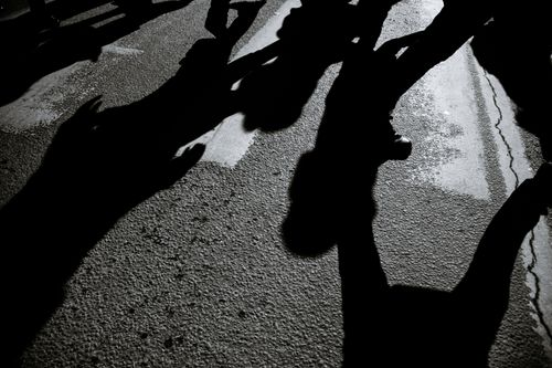 Free From above black and white of crop anonymous pedestrians walking on asphalt roadway with shadows in city Stock Photo
