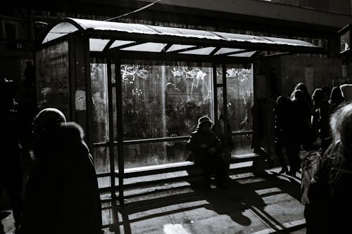 Free Black and white of crop anonymous people near roofed bus stop with glass wall on urban sidewalk Stock Photo