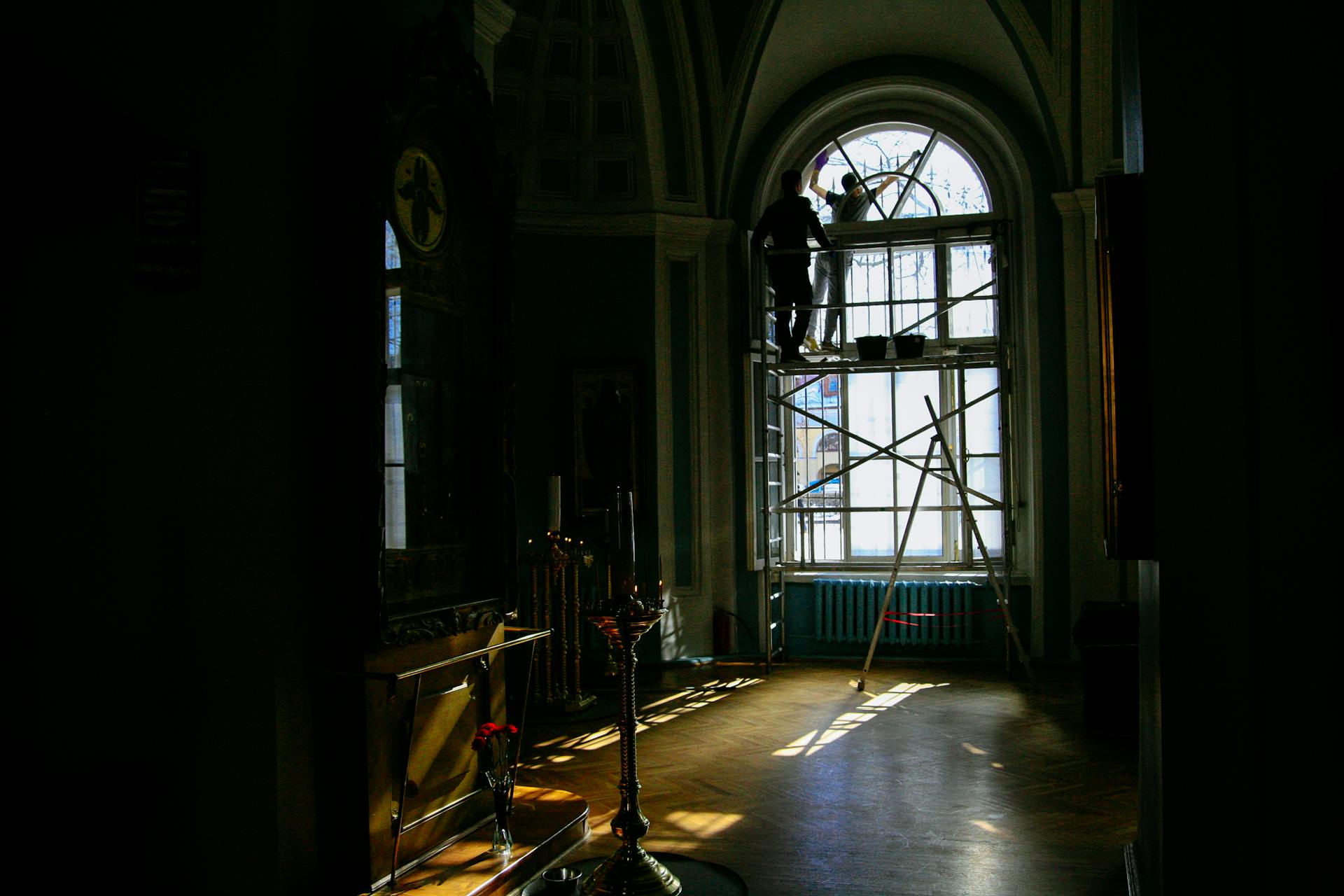 Back view of anonymous workmen on scaffold near arched window during restoration process in aged house