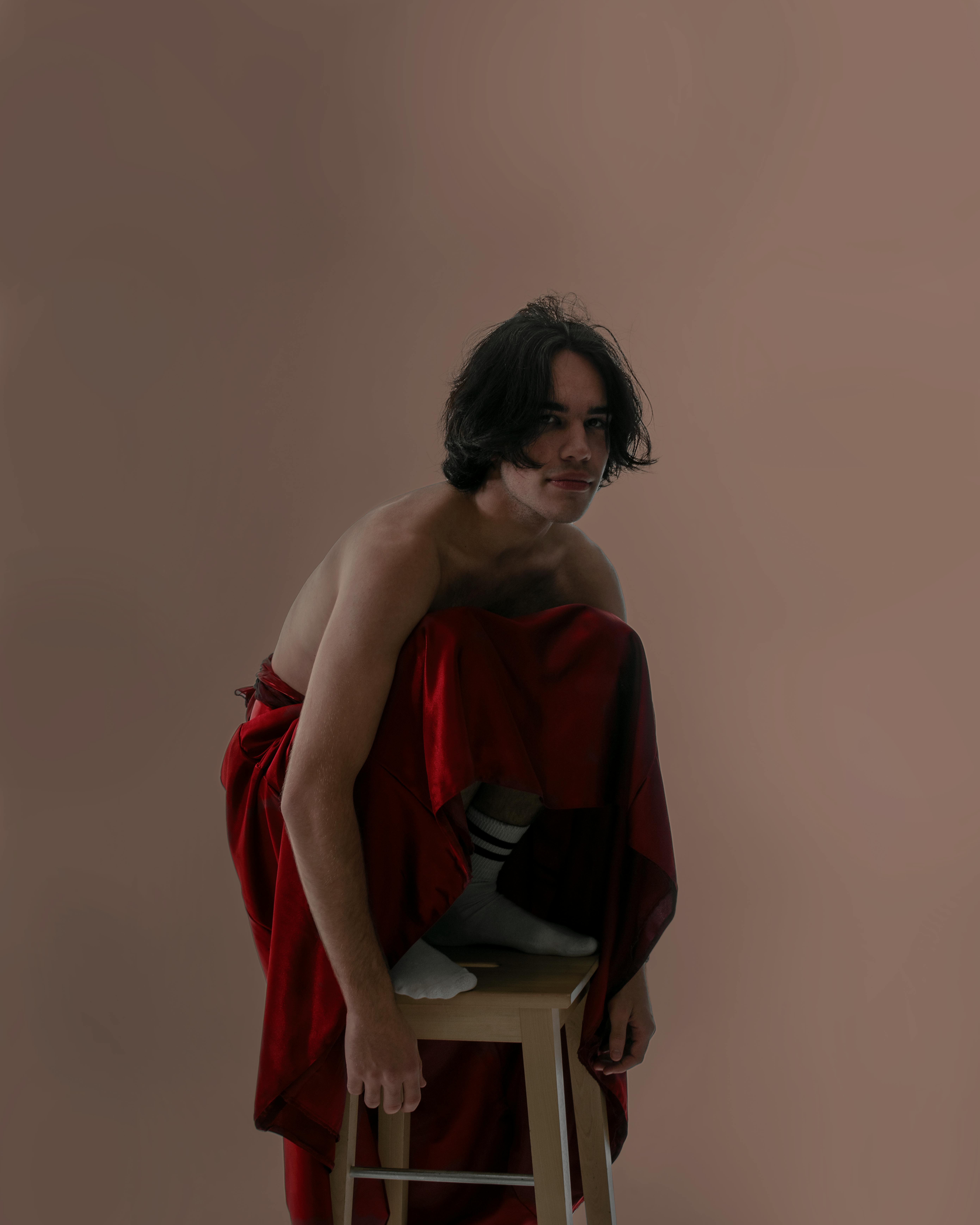 Striking image of a man sitting shirtless on a stool, enveloped in a long red cloth.