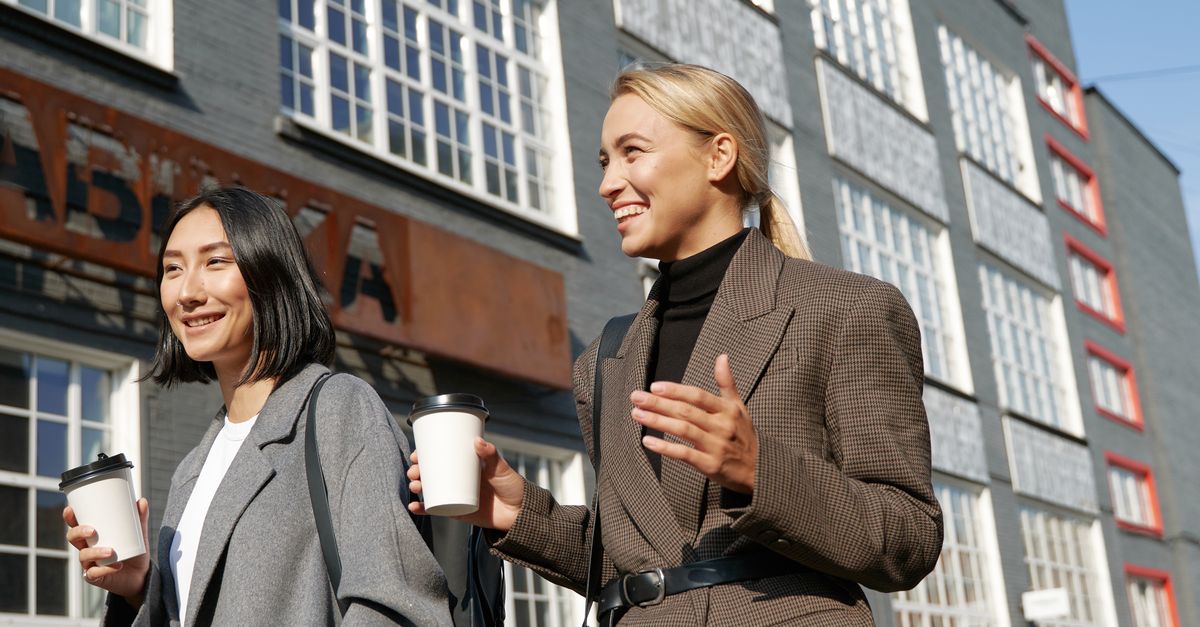 two people walking outside in the afternoon sun, laughing, office building in background