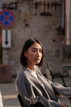 一位年轻女子穿着灰色外套，在柔和的阳光下坐在户外