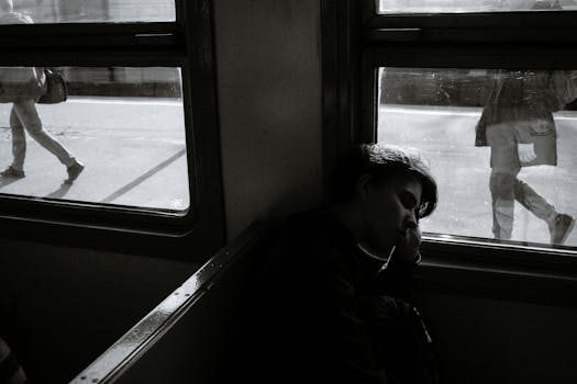 Black and white side view of anonymous female passenger on bench in electric train against urban platform with crop walking men