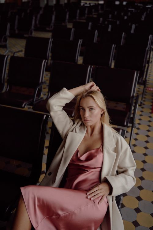 Free Elegant woman in a pink dress with white blazer, seated indoors with a stylish look. Stock Photo