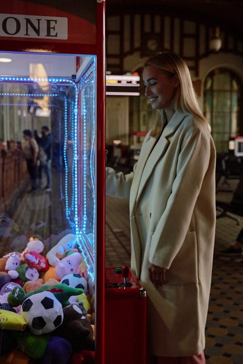 A Woman in White Coat Standing Beside the Arcade Game